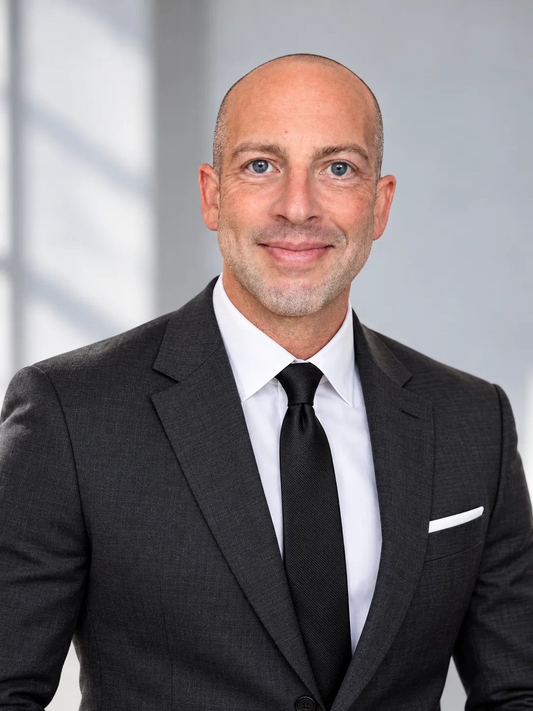 Tyler Barnett in a sharp charcoal suit, white shirt and black tie, looking directly at the camera